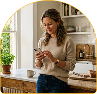 Woman in a kitchen checking her phone while holding a mug.