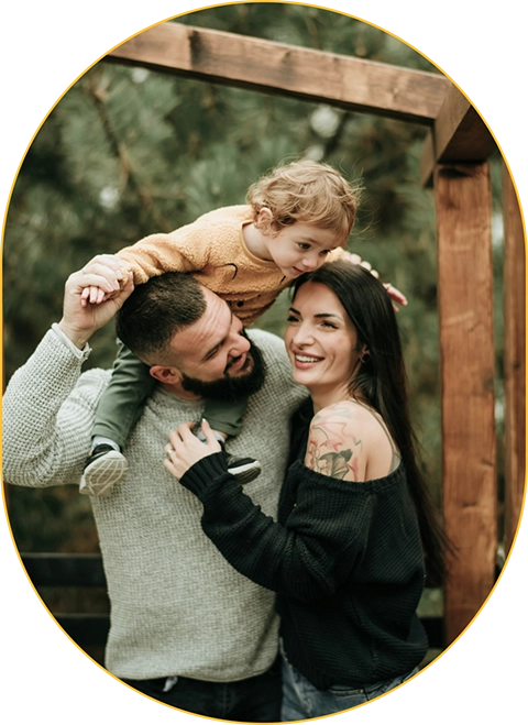 Family hugging and smiling with child on dad's shoulders.